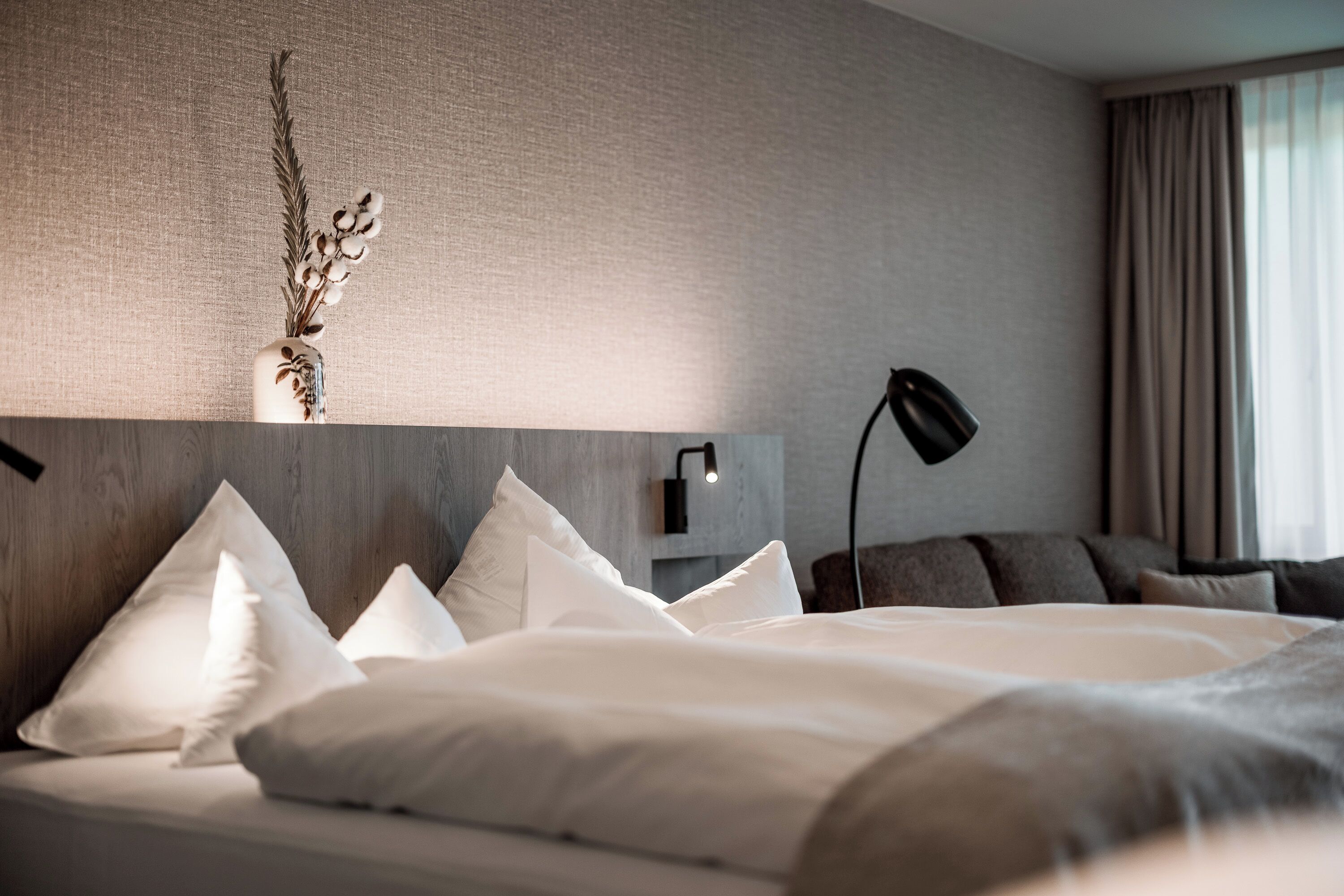 Une chambre d’hôtel avec un grand lit, plusieurs oreillers, une lampe fixée au mur et une plante décorative.