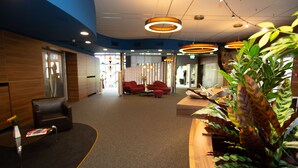Een moderne lobby met een gebogen receptiebalie, een zithoek en een grote plant.