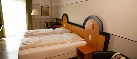Quarto de hotel com cama de casal, uma mesa, uma cadeira, luminária e um quadro na parede.