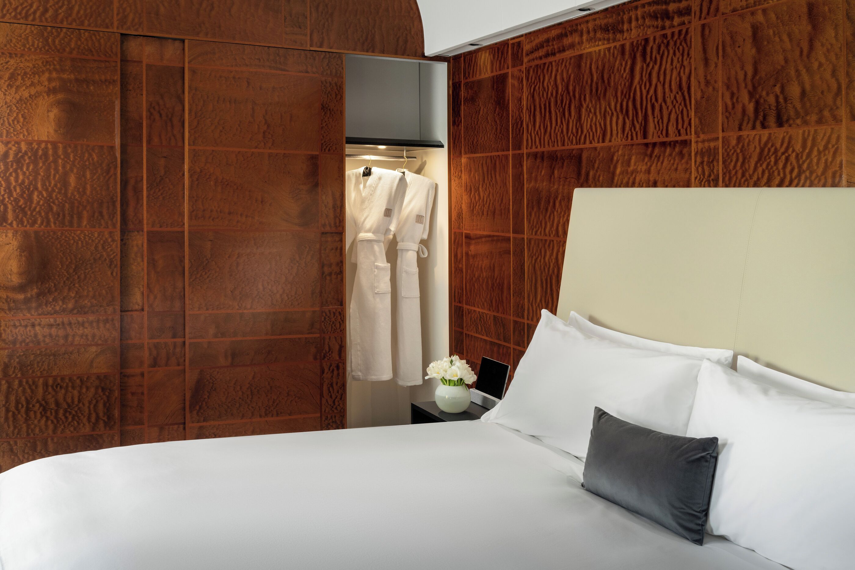 A hotel room with a bed, a nightstand with a vase of flowers, and a wooden wardrobe.