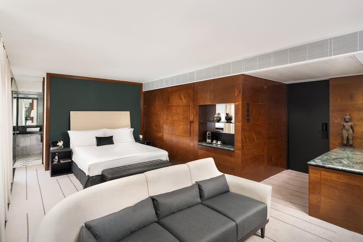 Une chambre d’hôtel moderne avec un grand lit, un canapé, un petit bureau et un miroir.
