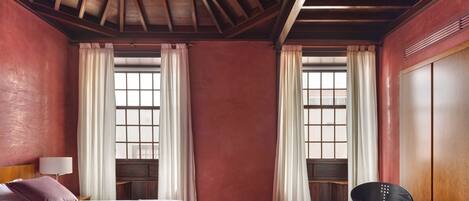 Een hotelkamer met een houten plafond, een bed met een witte dekbedovertrek, een glazen salontafel, een paarse stoel en een garderobe.
