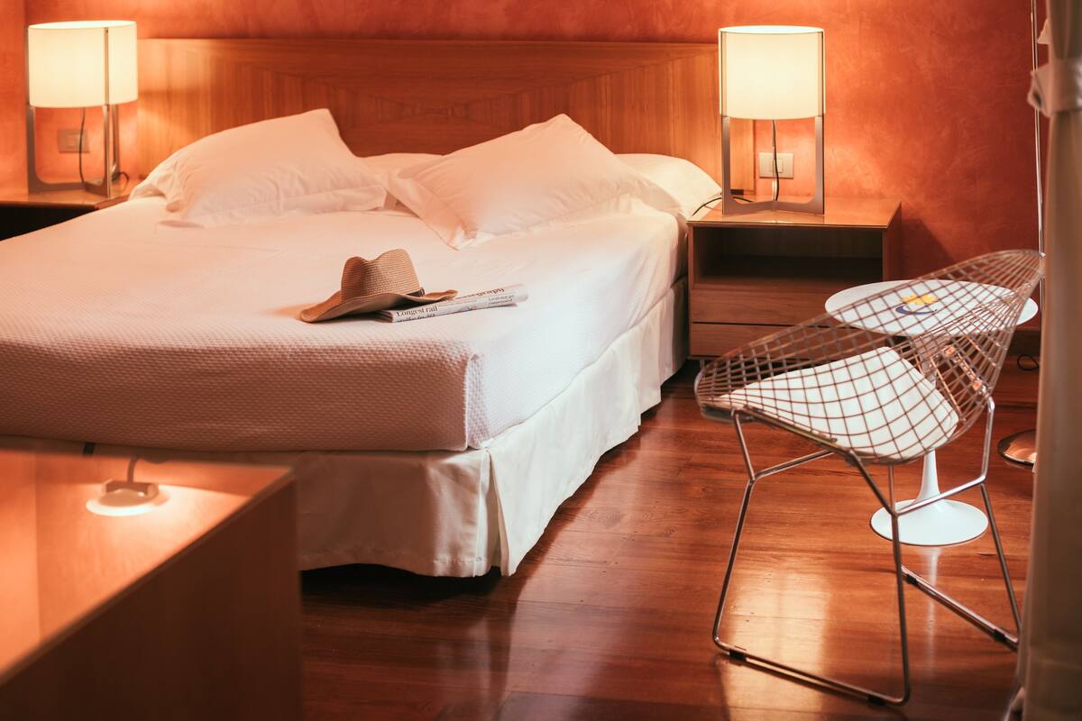 Una habitación de hotel con una cama bien hecha, dos lámparas de noche, una silla y una mesita de noche.