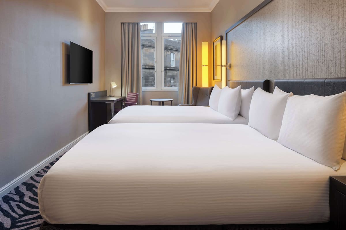 A hotel room with a large bed, a television, a small table, a chair, and a window with curtains.