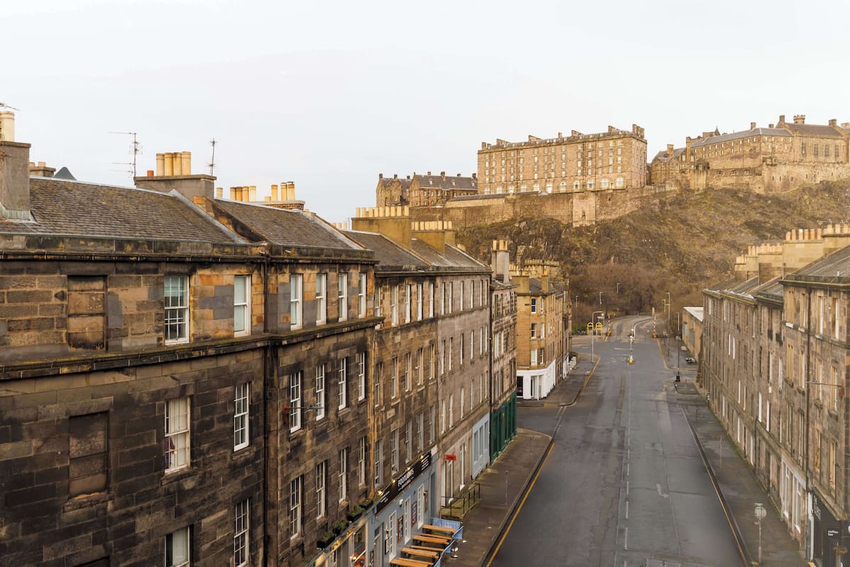 A street view with historic stone buildings and a castle in the background.