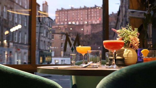 A table with drinks and a vase of flowers, set against a city view. - DoubleTree by Hilton Edinburgh City Centre (Edinburgh)