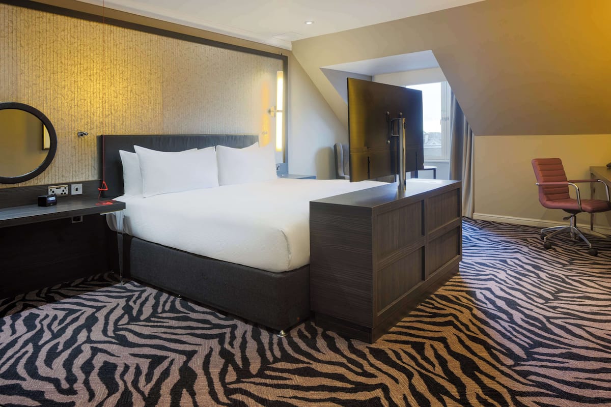 A hotel room with a large bed, a desk with a computer, a mirror, and a zebra-patterned carpet.