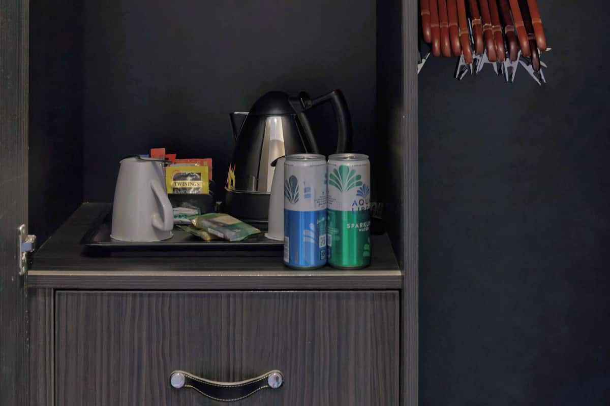 A dark-colored cabinet with a handle, containing a kettle, a box, and two cans of water.