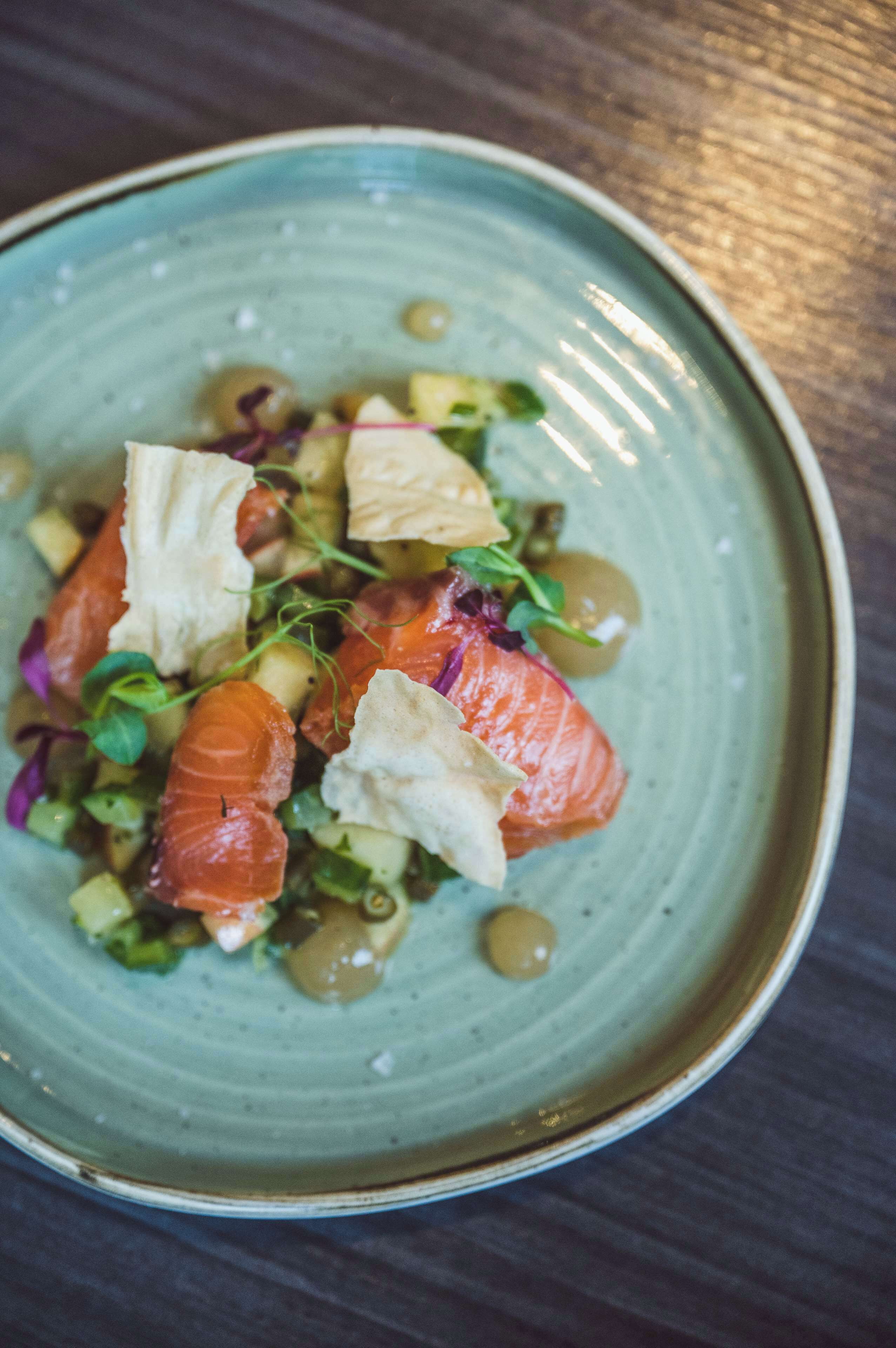 A plate of food with salmon, greens, and other ingredients.