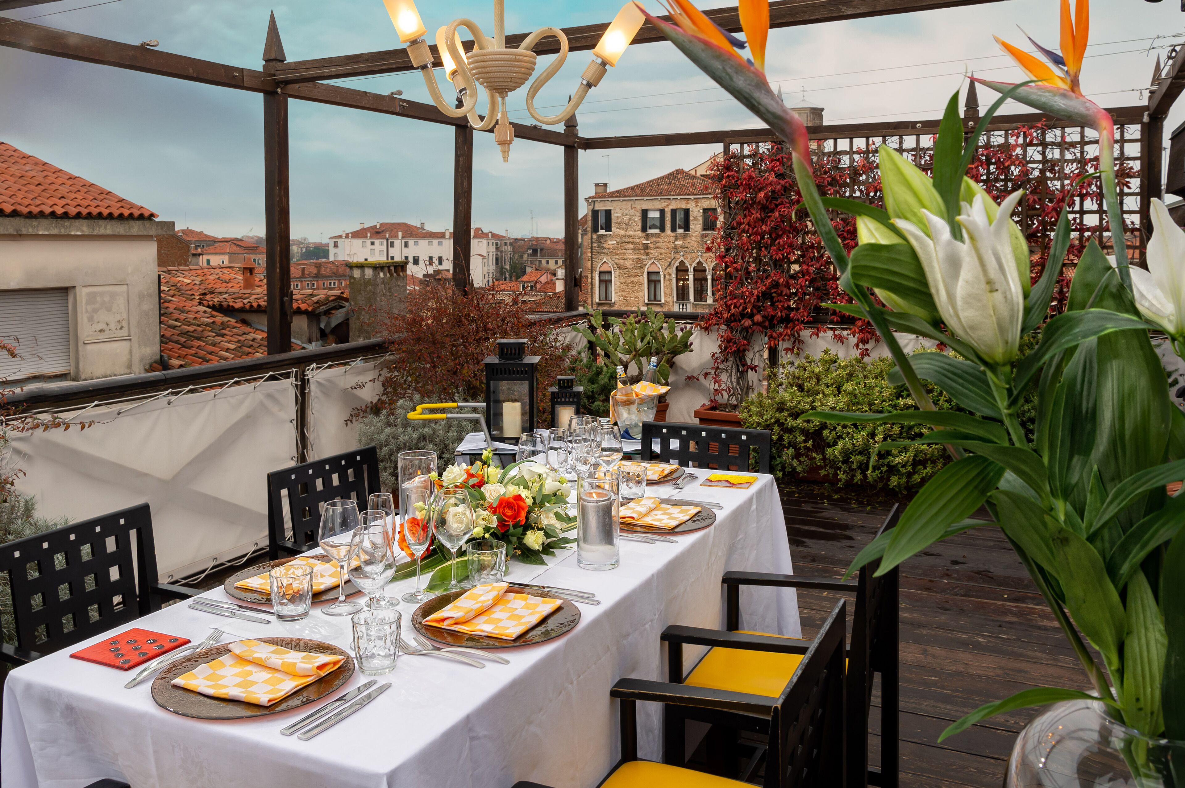 An outdoor dining area with a table set for a meal, surrounded by chairs and a view of buildings in the background.