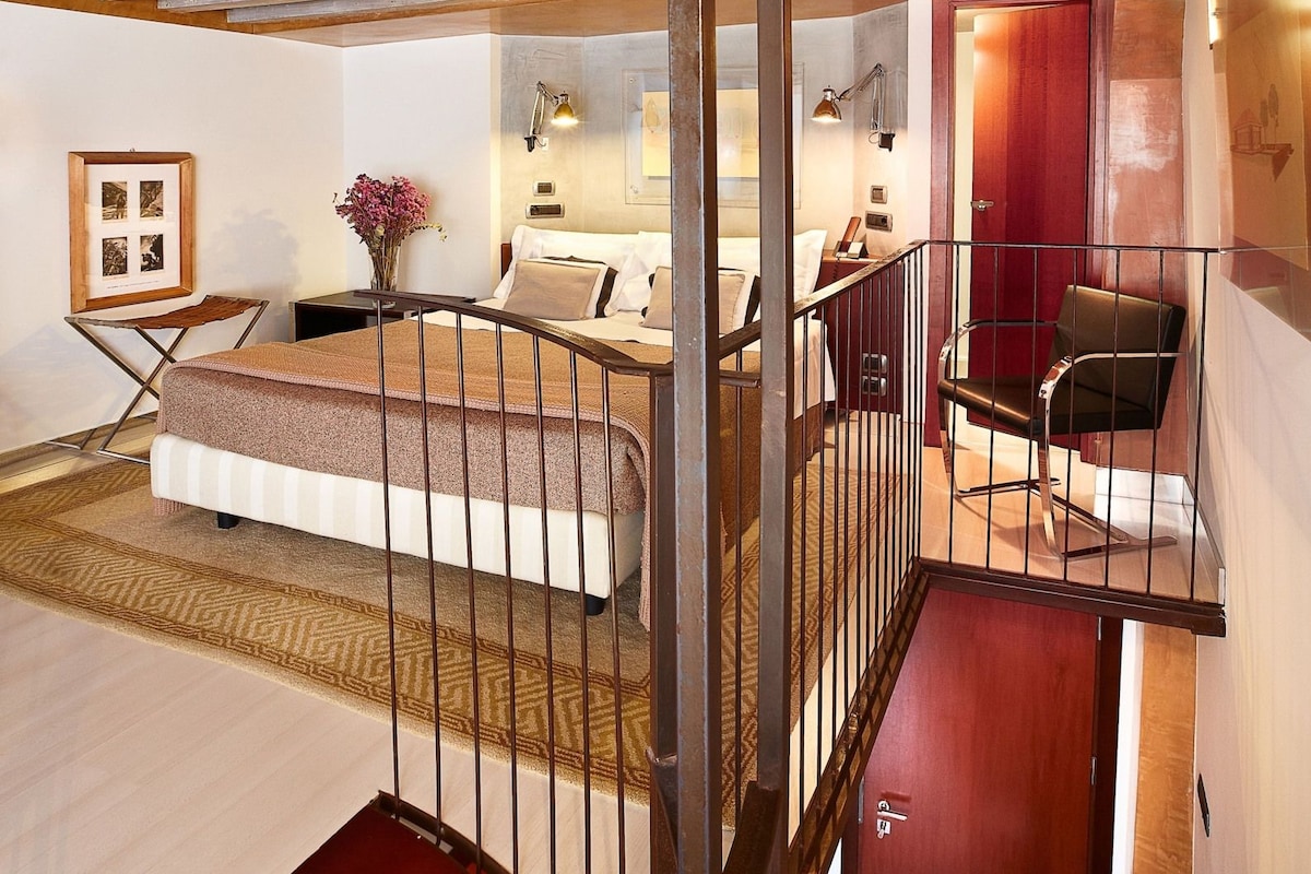 A hotel room with a bed, a desk, a chair, a staircase, and a door.