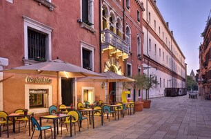 Un caffè all'aperto con tavoli e sedie, un edificio con insegna da ristorante-bar e cielo sereno.