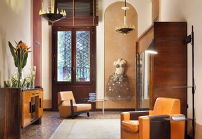 Una hall moderna con un mobile in legno, un'area salotto con poltrone arancioni, una scultura decorativa e un'ampia finestra vista alberi.