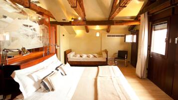 A hotel room with a large bed, a desk with a lamp, a chair, and a wooden ceiling.