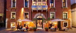 En hotels facade med udendørs siddepladser og en midterindgang.