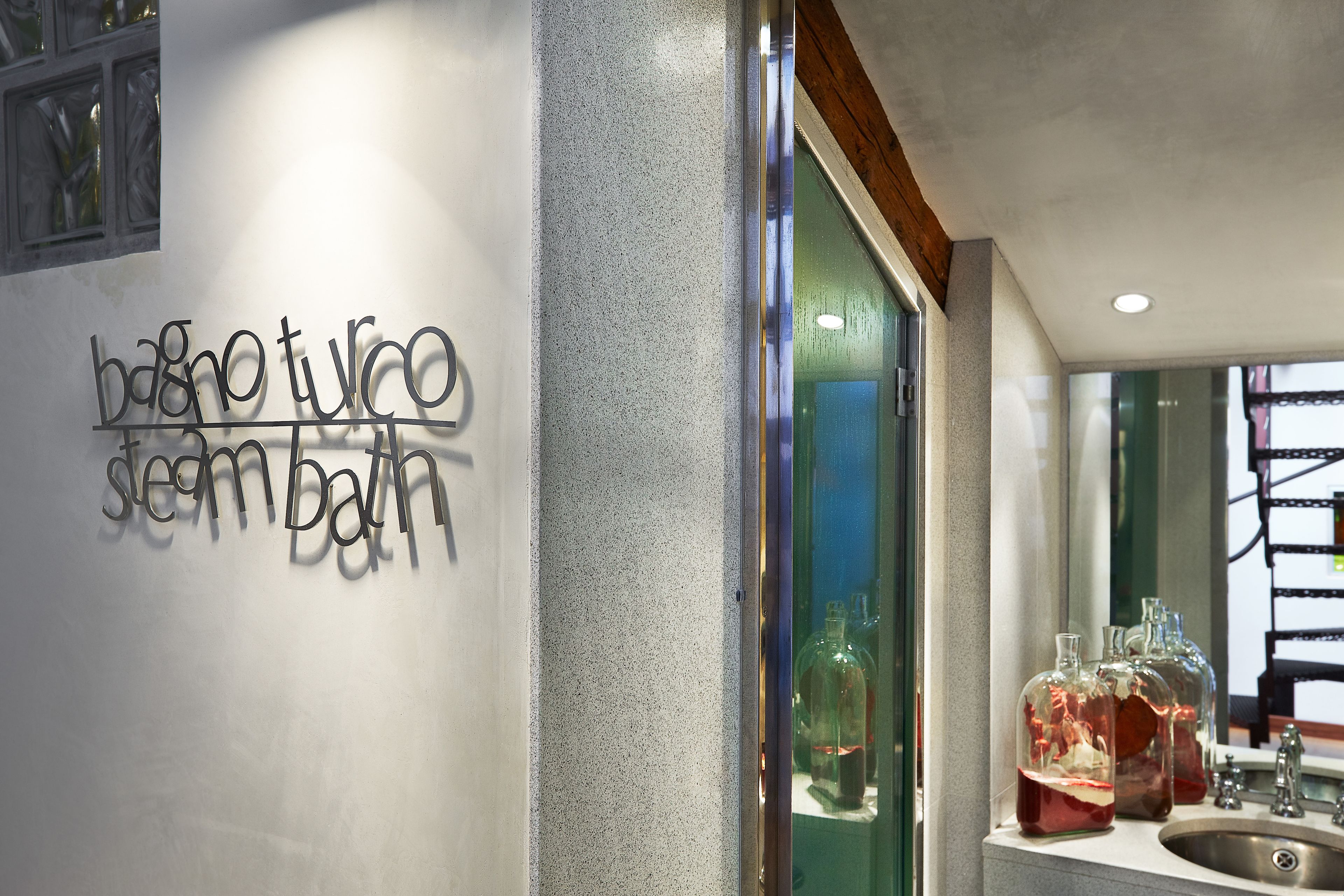 A bathroom with a sign reading "banyo tuco steam bath" and a sink with glass bottles.