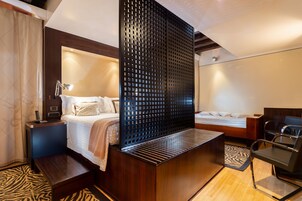 Una camera d'albergo moderna con un letto, comodini, una lampada e un angolo salotto con una sedia e un tavolo.