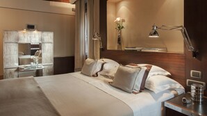 A modern hotel room with a large bed, a bedside table with a lamp, a mirror, and a vase with flowers.