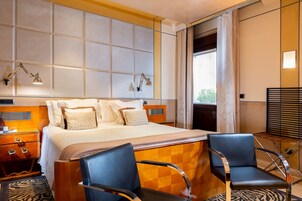 A hotel room with a large bed, two bedside tables, a desk with a chair, a zebra-patterned rug, and a window with curtains.