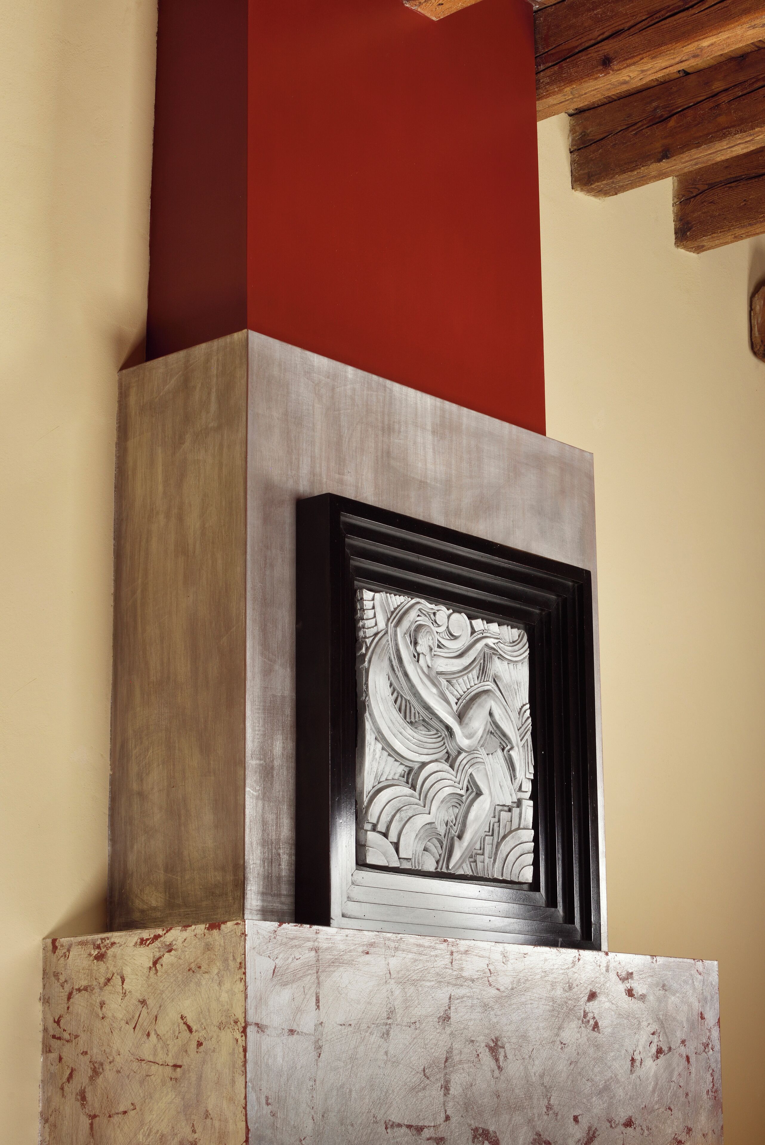 Une cheminée ornée de sculptures complexes, une console en bois et un mur rouge au-dessus.