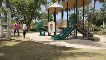 Un parque infantil con toboganes y estructuras para escalar, rodeado de árboles y un cielo despejado.