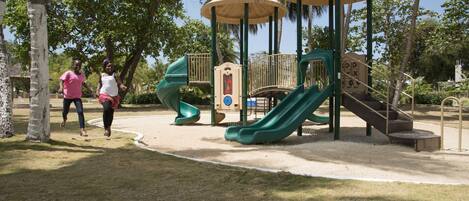 Un parque infantil con toboganes y estructuras para escalar, rodeado de árboles y un cielo despejado.