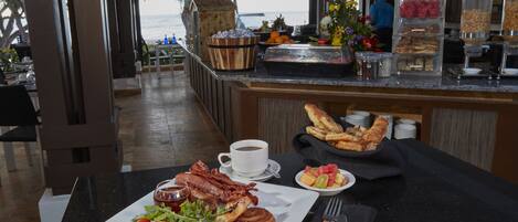 A breakfast buffet with a variety of food items, a coffee cup, and a view of the ocean.