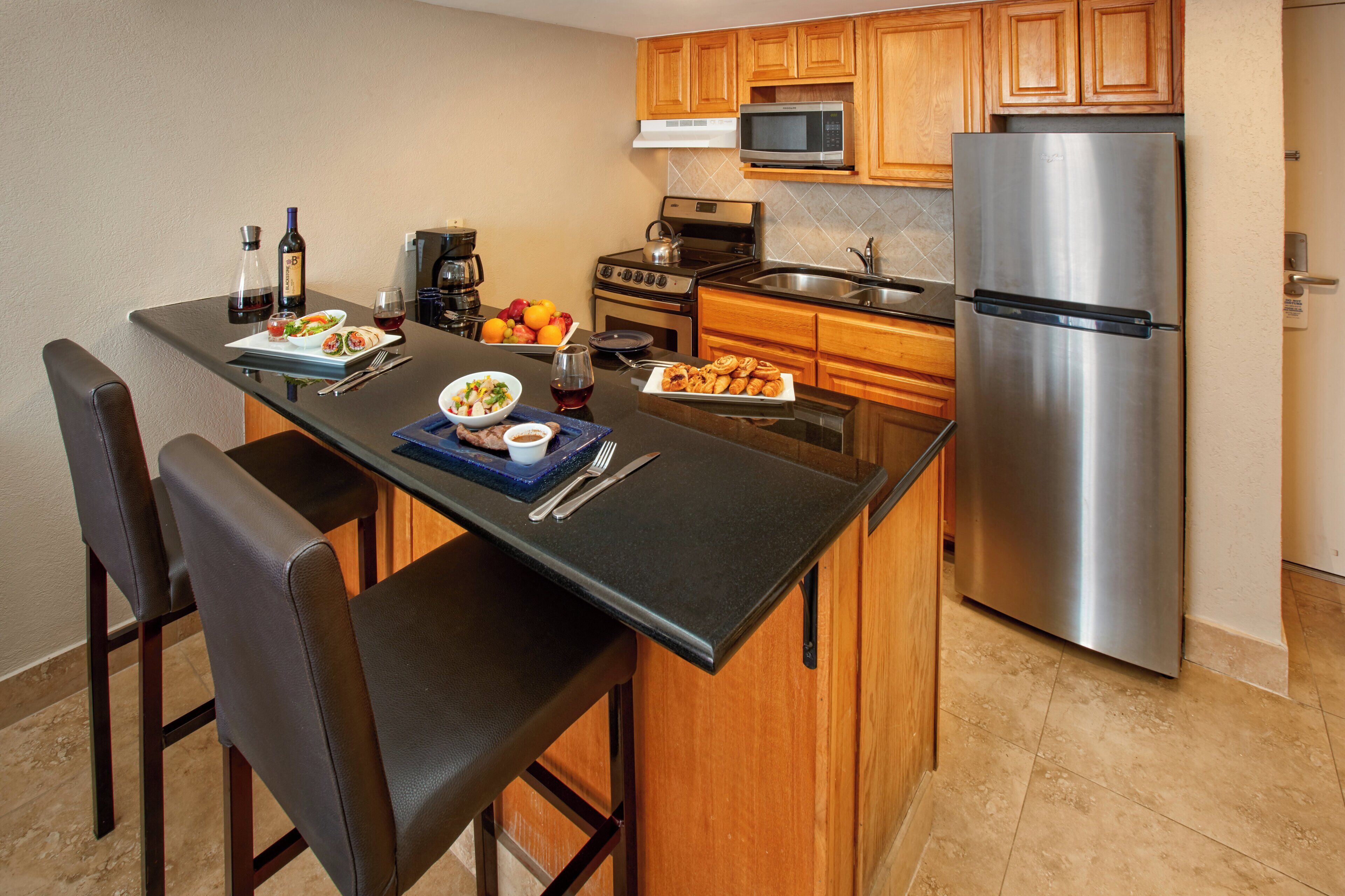 A kitchen with wooden cabinets, a stainless steel refrigerator, a microwave, and a stove.