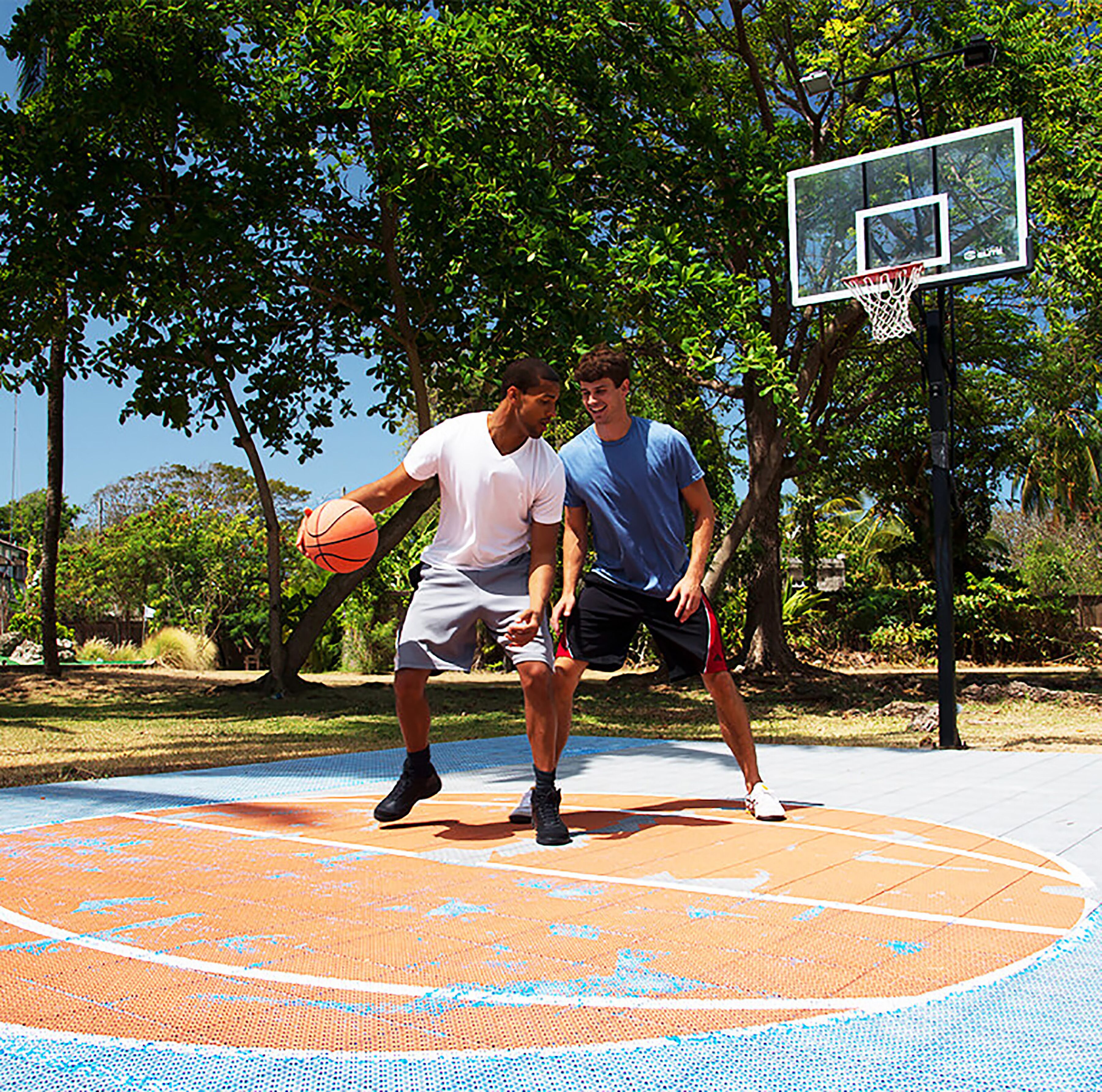 Two people playing basketball on an outdoor court with trees in the background.
