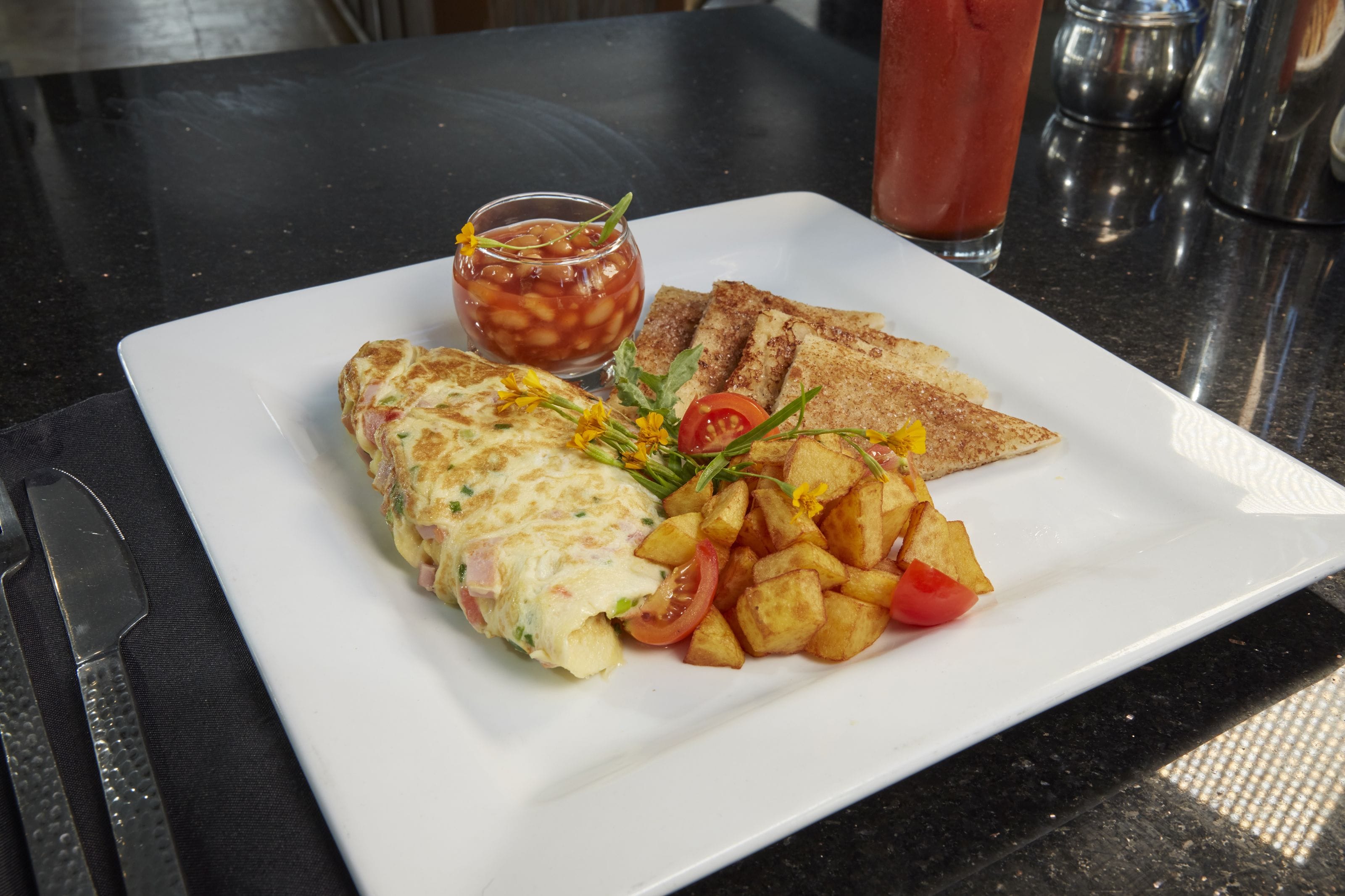 A breakfast plate with an omelette, toast, roasted potatoes, and a side of tomato sauce.