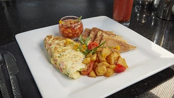 A breakfast plate with an omelette, toast, roasted potatoes, and a side of tomato sauce.