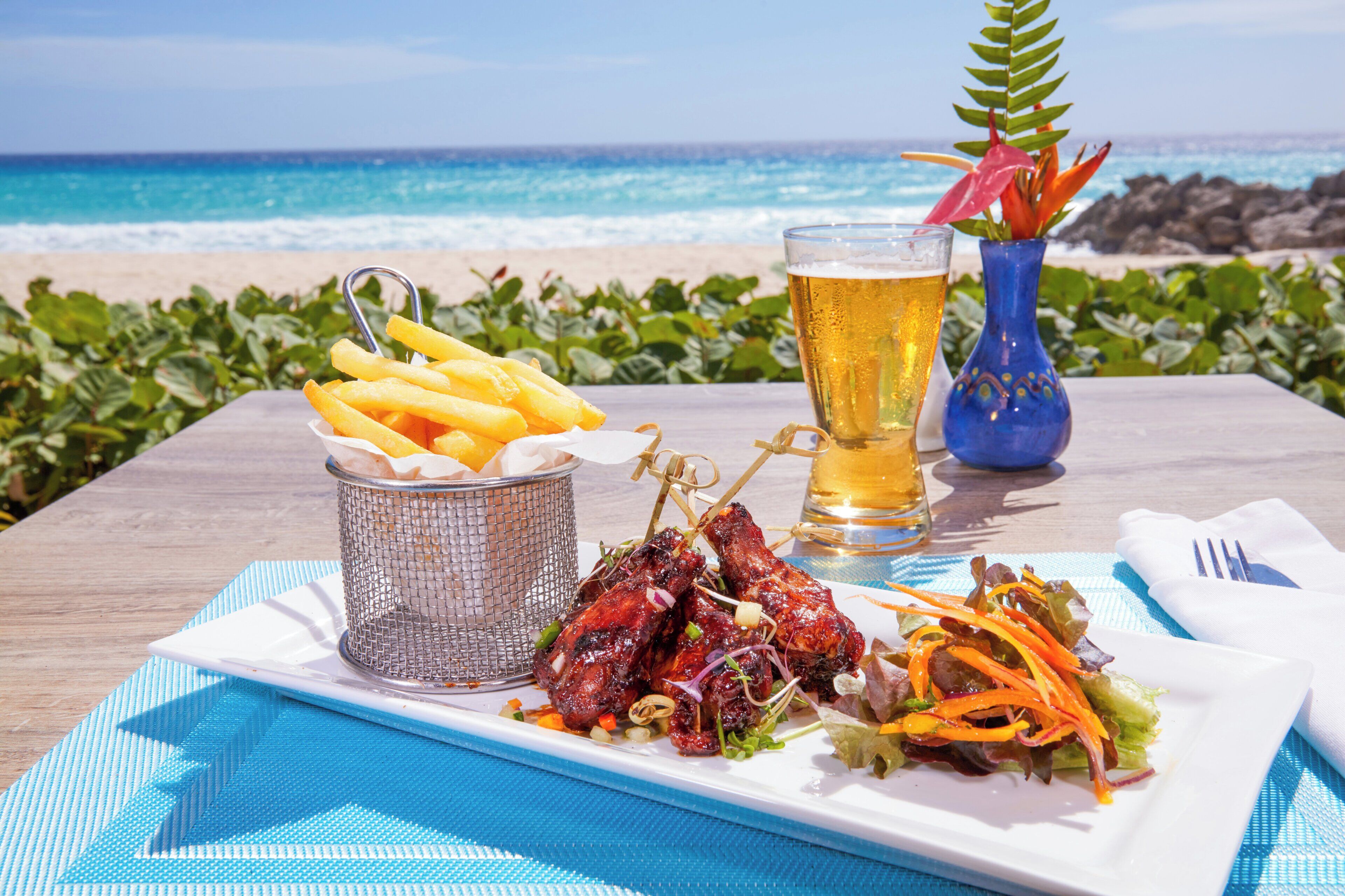 A meal with fries, ribs, and salad on a table with a view of the beach and ocean.