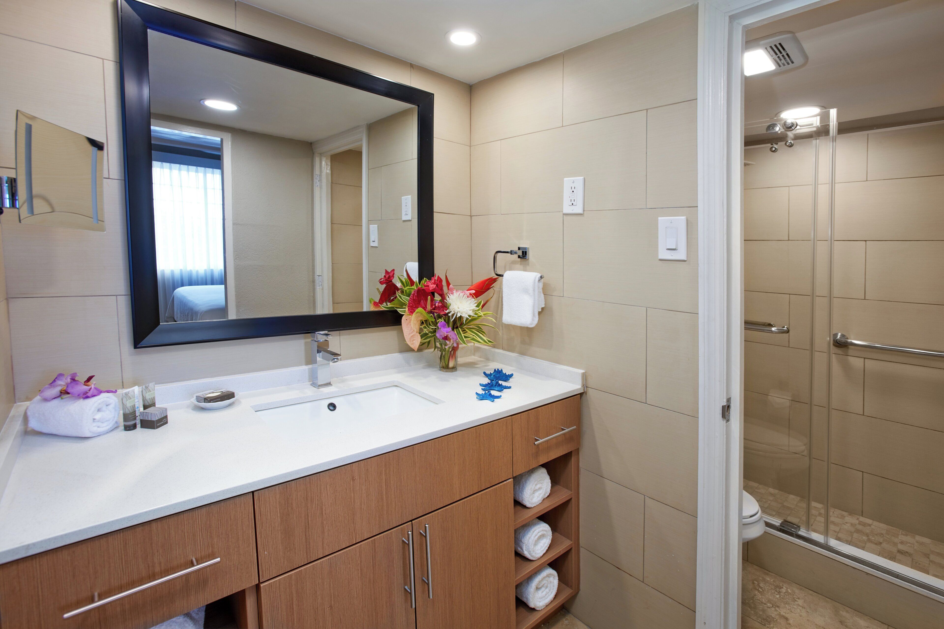A bathroom with a large mirror, a sink, a shower, and a towel rack.