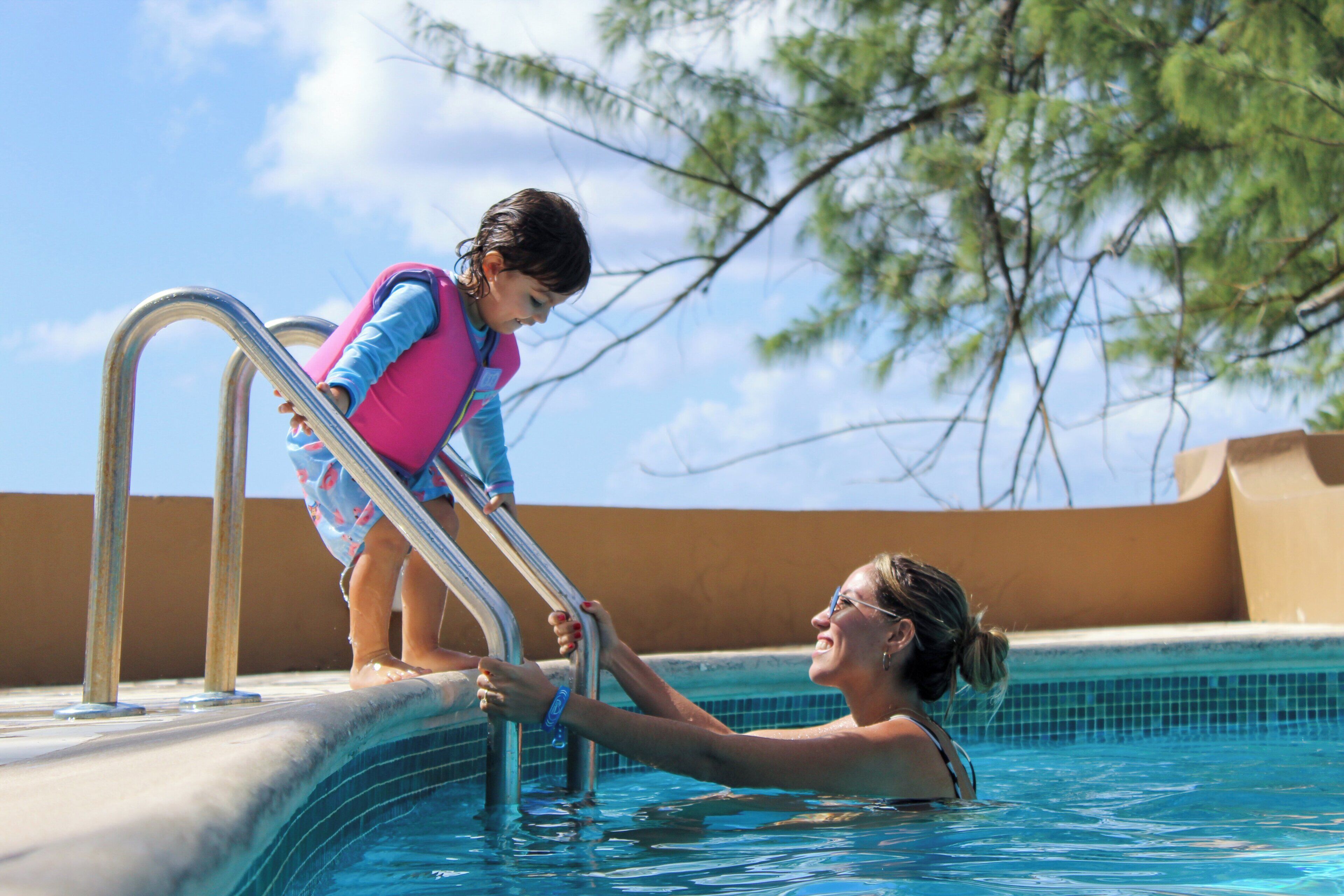Una piscina con una scala in metallo, acqua cristallina e un bambino in piedi sulla scala.