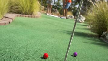 A miniature golf course with two balls near the hole, palm trees, and a person in the background.