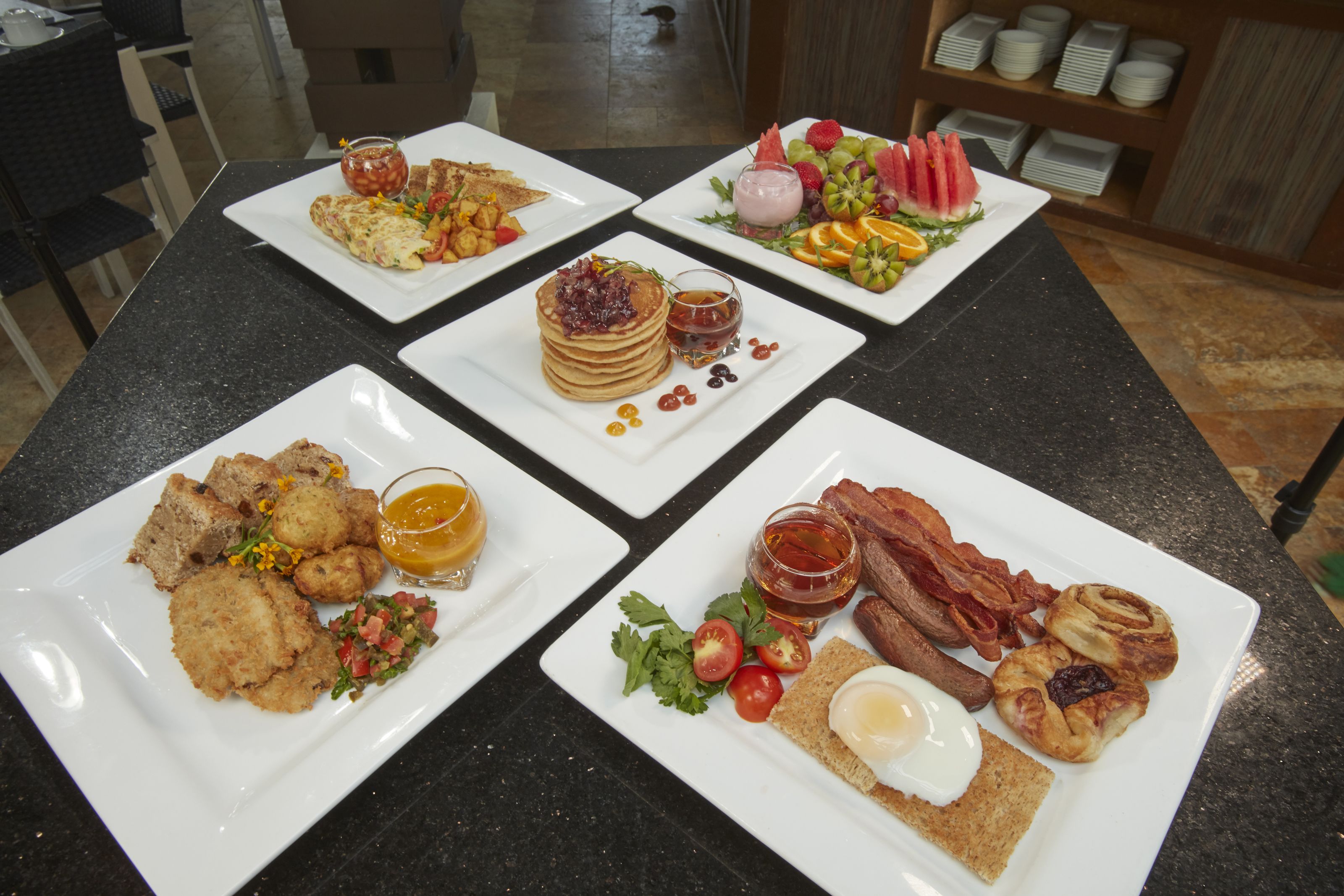 Un bufé de desayuno con diversos platos, como panqueques, tocino, huevos y fruta.