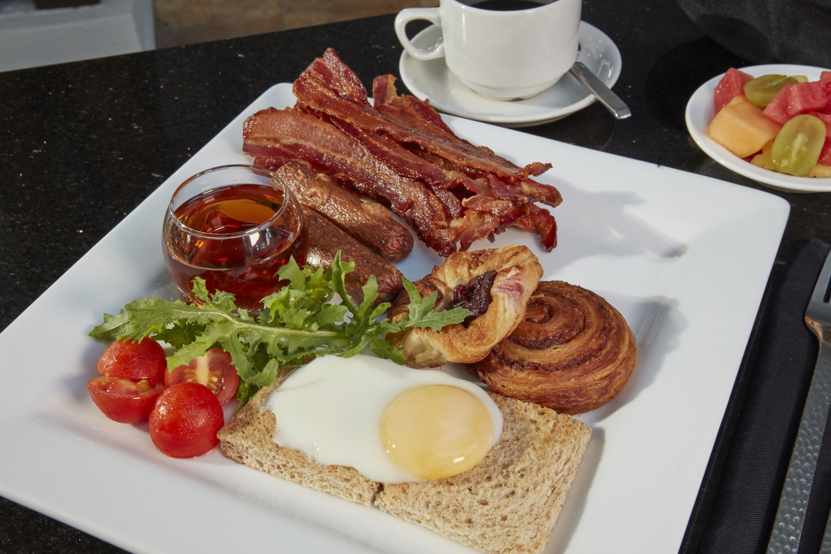 Un plato de desayuno con tocino, huevos, tostadas y tomates.