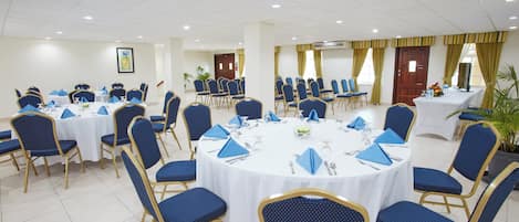 Un salón de conferencias con mesas redondas, sillas azules y manteles blancos.