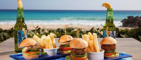 A table with food and drinks on a beach with ocean in the background.