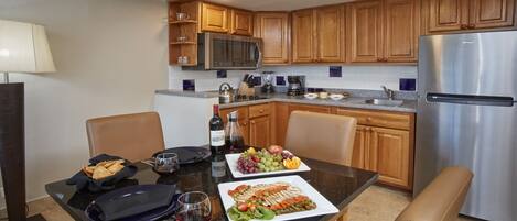Una cocina moderna con armarios de madera, un refrigerador de acero inoxidable y una mesa de comedor dispuesta con platos, vasos y una botella de vino.