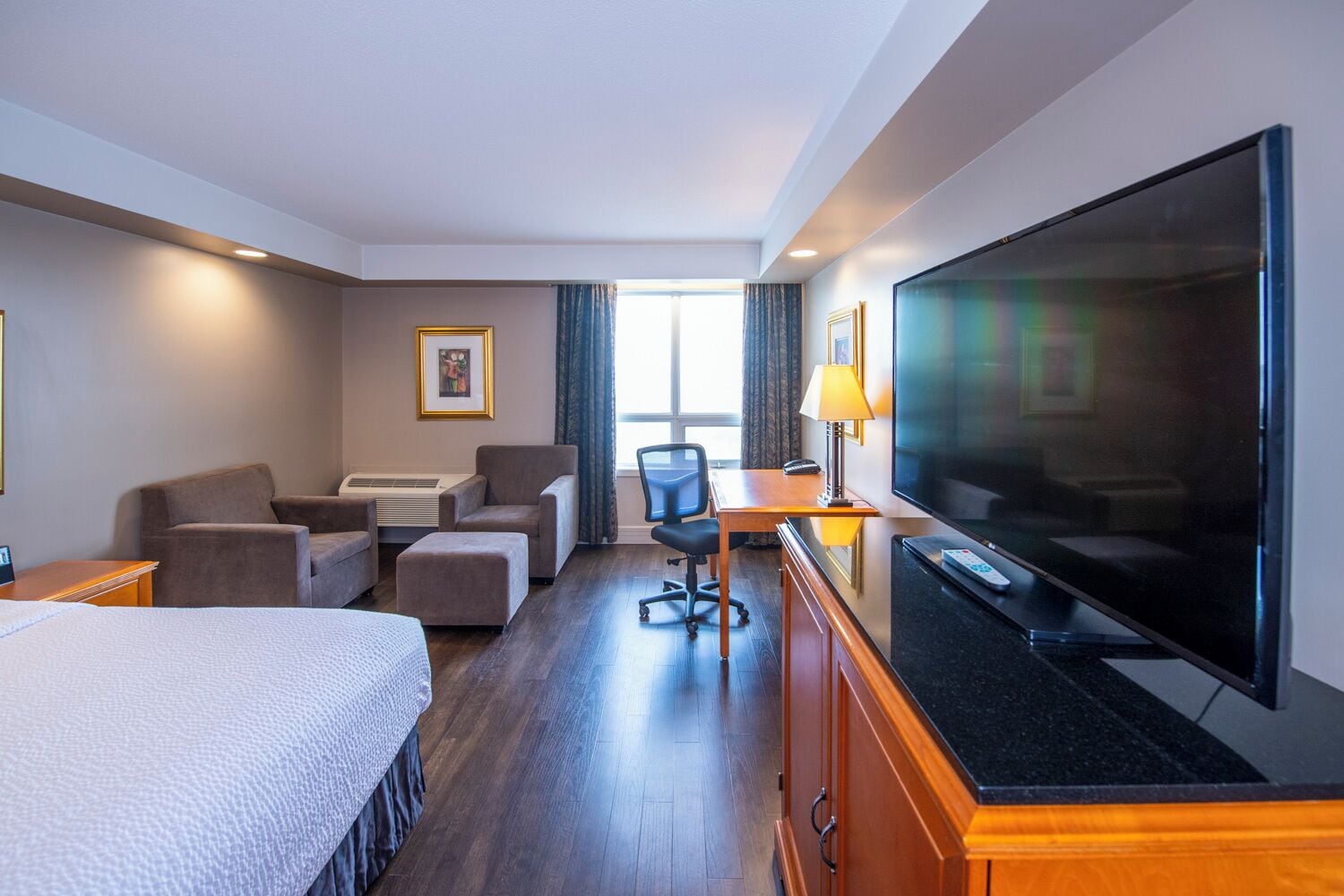 A hotel room with a bed, a desk with a chair, a television, and a large window.
