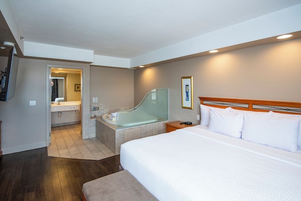 Une chambre d’hôtel avec un lit, une salle de bain avec une baignoire et une tête de lit en bois.