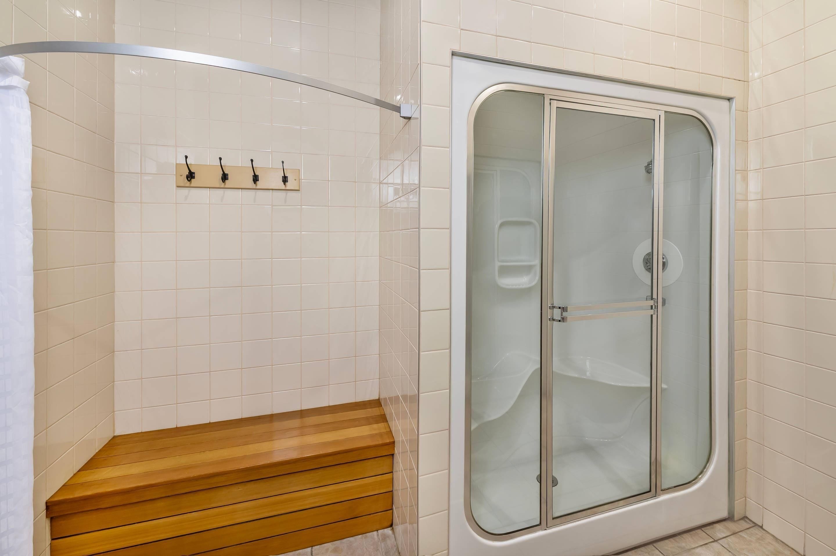A shower with a glass door, a wooden bench, and a towel rack with hooks.