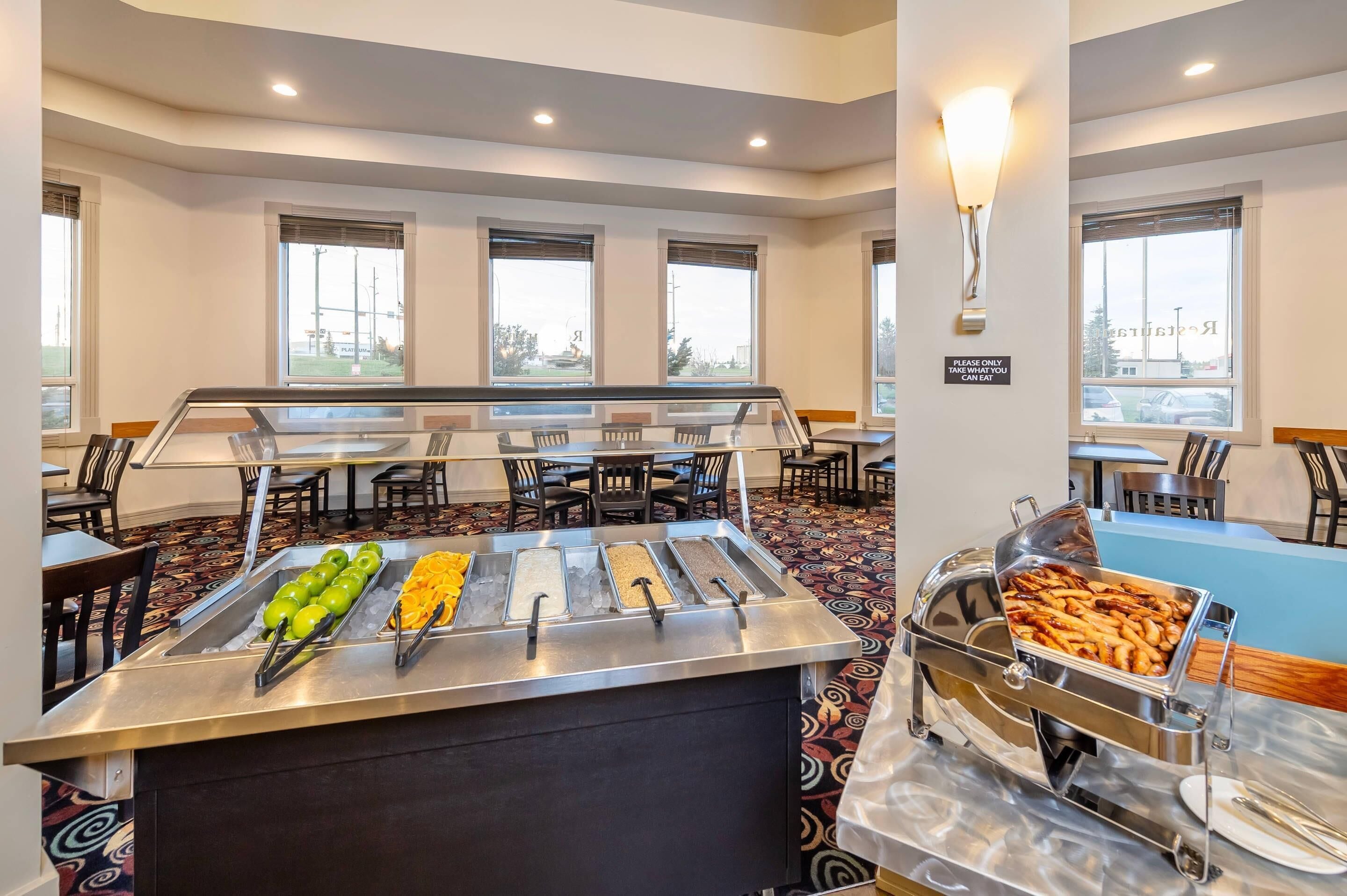 A buffet area with various food options, including fruits and meats, in a hotel setting with multiple tables and chairs.
