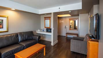 A modern living room with a leather sofa, a wooden coffee table, a gray armchair, and a flat-screen TV.
