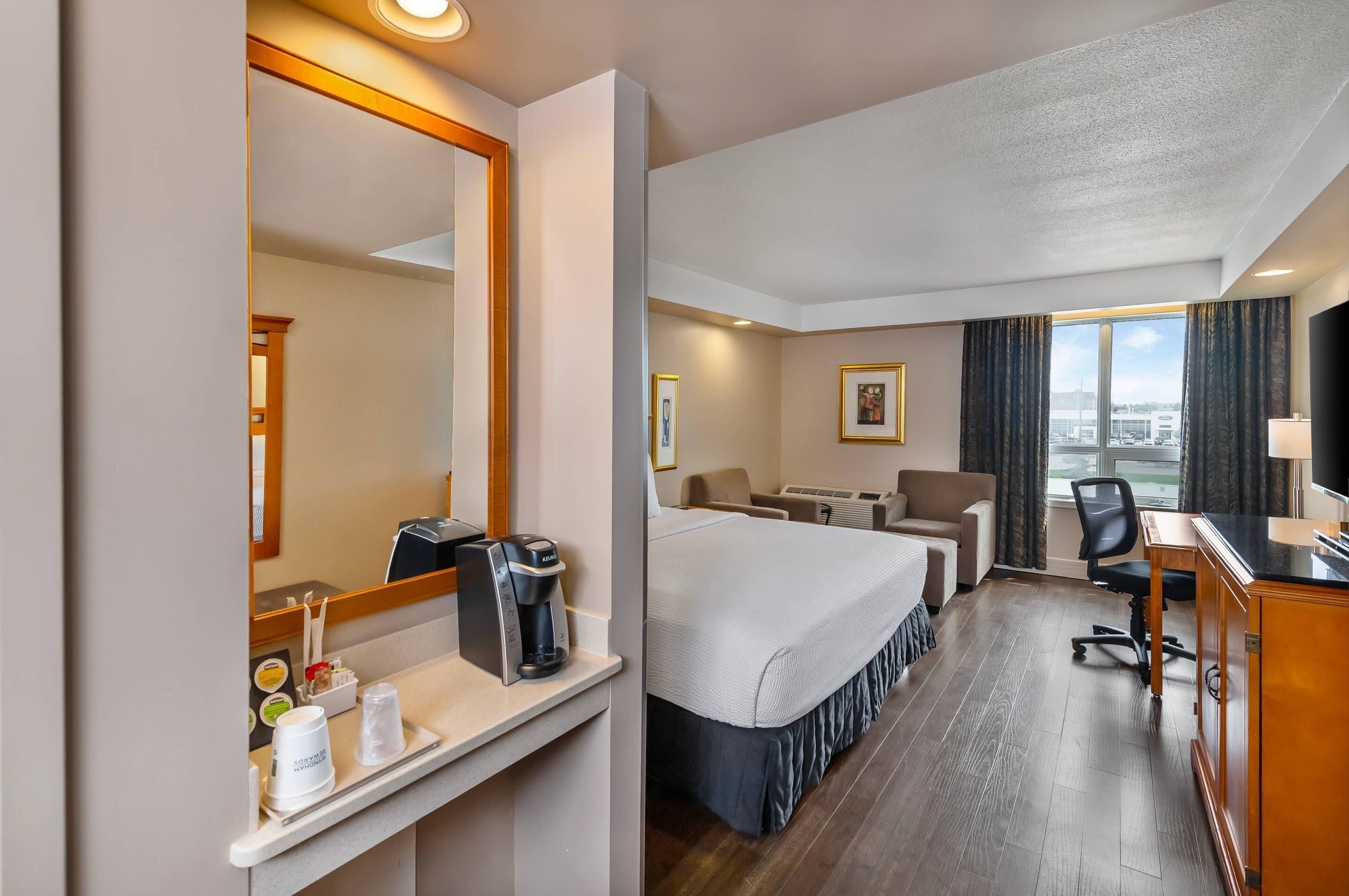 A hotel room with a bed, desk, chair, and a large window with a view.