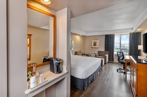 A hotel room with a bed, desk, chair, and a large window with a view.