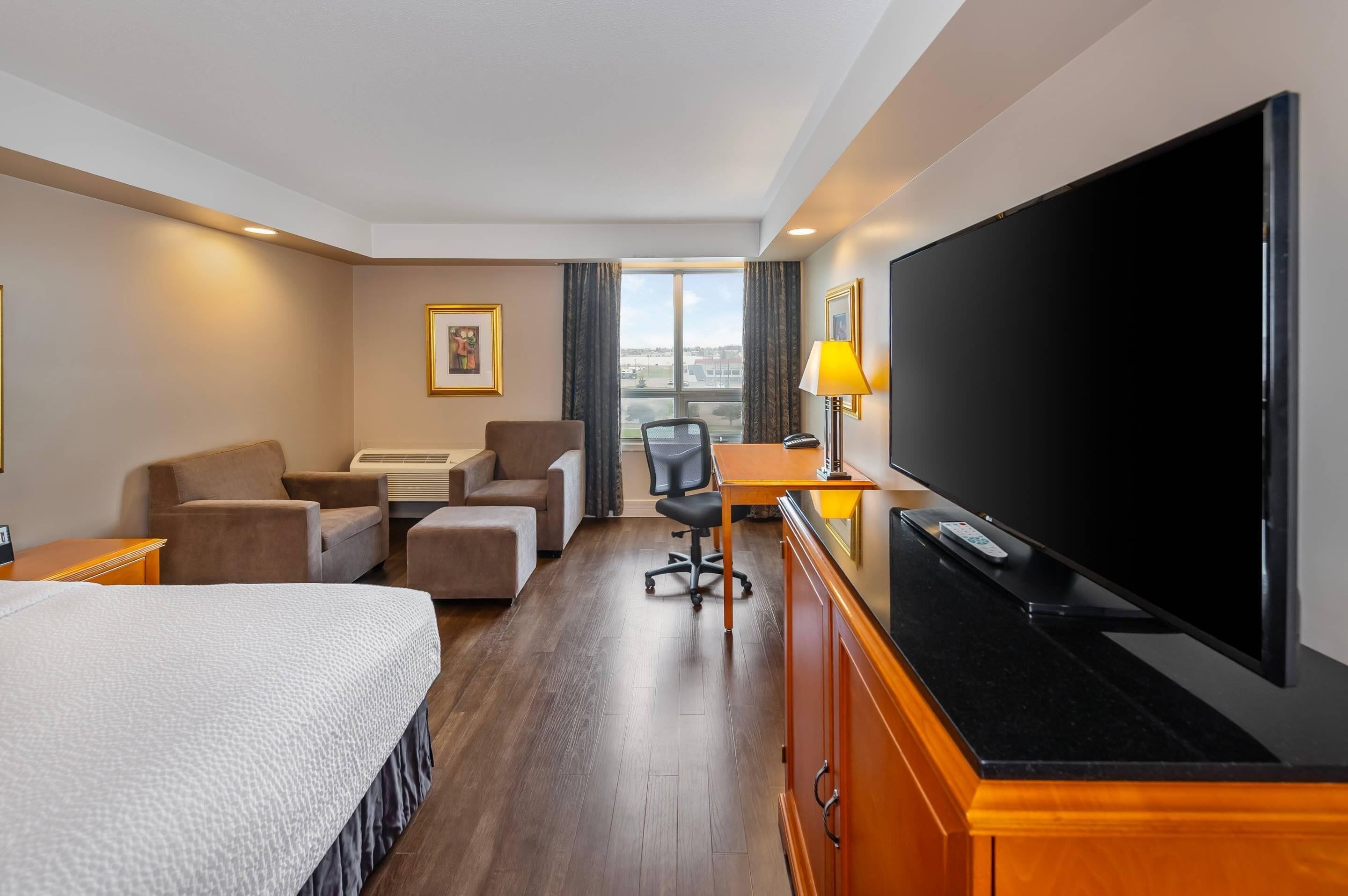 Habitación de hotel con cama, escritorio, silla, televisor y ventana con vistas.