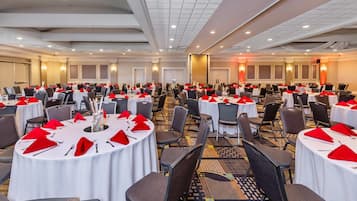 Une grande salle de conférence équipée de plusieurs tables rondes, chacune agrémentée de serviettes rouges et de couverts en argent.