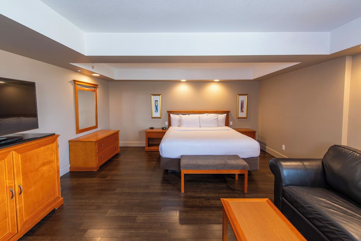 A hotel room with a bed, a television, a wooden dresser, a leather couch, and a small table.